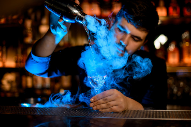 professional-male-bartender-pouring-smoke-into-cocktail-glass-from-shaker-blue-light_130488-781